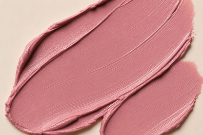 A close-up of a dusty rose pink cosmetic cream swatch, showing the thick, creamy texture and smooth swipe strokes on a light beige background.